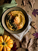 Set of dried autumn leaves and cloth napkins placed on lumber tabletop near bowl with yummy pumpkin hummus with seeds and seasame