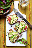 Slices of bread topped with avocado, figs, pistachio nuts, thyme and wild herb salad