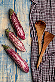 Set of fresh ripe eggplants placed near piece of striped cloth on weathered wooden tabletop