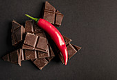 Pieces of yummy chocolate placed with chili pepper on dark background