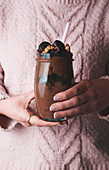 Woman in pink sweater holding glass of chocolate smoothie with nuts and candies
