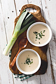 Two bowls of tasty Vichyssoise soups on wooden table with leek