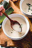Hand with spoon and tasty Vichyssoise soup on wooden table with leek