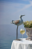 Bird ornament and glass of white wine on table with sea in background