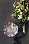 Bouquet of hellebores tied with dark ribbon and pewter plate on dark surface
