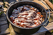 A pot being lined with bacon and layered with meat, onions and peppers