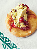 A cracker topped with cheese and pomegranate seeds