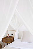 Rustic bedside table next to the bed with white canopy