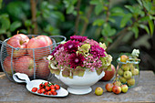 Gesteck aus Hortensien, Fetthenne und Chrysanthemen, daneben Äpfel und Zieräpfel