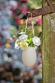 Petunias and rose in suspended egg used as vase