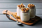 Glass bottles with cold tasty milk and natural delicious walnuts with spoon on wooden tray