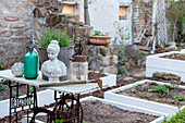 Bust of woman and vintage bottles on table next to freshly prepared raised beds in garden