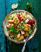 Oriental bowl with couscous, hummus, pollack, pomegranate seeds and mint