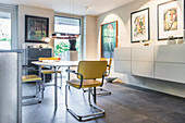 Round table, cantilever chairs, floating sideboard and artworks on wall in open-plan dining area