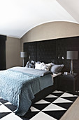 Doppelbett vor schwarzen, gepolsterten Paneelen im Schlafzimmer, schwarz-weißes Teppich