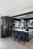 Display cabinet, island counter and black walls in elegant open-plan kitchen