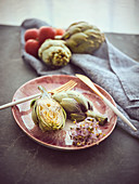 Small knife and fork and cut and whole fresh artichokes placed on pink ceramic plate on table