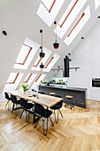 Island counter with bar stools and dining table with black chairs in high-ceilinged room with skylights in sloping wall