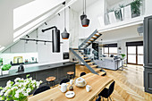 Island counter, dining area and staircase in high-ceilinged room with skylights in sloping wall