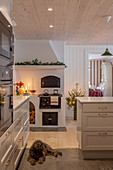 Dog lying on floor of festively decorated, white kitchen with wood-burning cooker