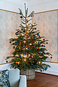 Christmas tree in corner against panels of patterned wallpaper surrounded by moulding