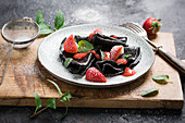 Vegane schwarze Crepes mit Erdbeersauce, frischen Früchten und Minze