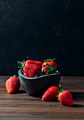 Fresh ripe strawberries in black concrete bowl on wood background