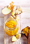Pineapple and onion chutney with curry and fresh ginger in a jar on a wooden surface