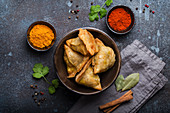 Indian samosas - fried pastry with savoury filling, served in bowl with spices and fresh cilantro