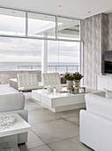 Modern living room decorated entirely in white with sea view through glass wall