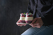 Woman holding in hands homemade classic dessert Panna cotta with raspberry and blueberry berries and jelly in jars