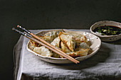Fried asian dumplings Gyozas potstickers in white ceramic plate, bowl of soy onion sauce