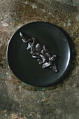 Peeled cloves of Black fermented garlic on ceramic plate over dark metal background