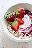 A bowl filled with yogurt, topped with strawberries, oats, and berry puree