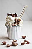 A white cup filled with vanilla ice cream topped with chocolate peanut butter candies