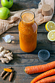 Bottle of fresh smoothie with ginger root and raw carrot placed on lumber table