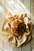 A freshly baked round loaf of bread on tea towel