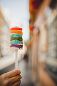 Hand holding baked tasty sweet rainbow cake and walking on city street