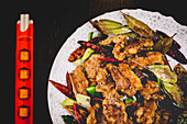 Cooked appetizing spicy lamb with cucumber, chili peppers and leaves on plate with chopsticks in Asian cafe