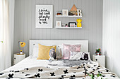 Weißes Doppelbett mit dekorativem Plaid und Zierkissen vor grauer holzverkleideter Wand