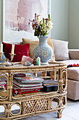 Magazines, games and vase of flowers on vintage-style rattan table in front of sofa