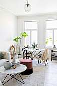 Couch, coffee table and pouffe in front of dining area in white interior with stucco ceiling