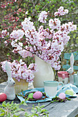 Easter table with bouquet of ornamental cherry, Easter eggs and Easter bunnies as decoration