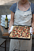 Frau hält Backblech mit frisch gebackener Focaccia