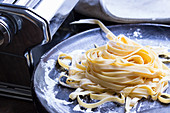 Homemade pasta on a plate in front of a pasta machine