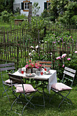 Gedeckter Gartentisch mit Klappstühlen in sommerlichem Bauerngarten