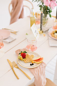 Waffles and fruit on table festively set in delicate pink shades