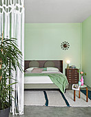 Schlafbereich mit Doppelbett und hellgrünen Wänden in Loftwohnung abgetrennt mit Fadenvorhang