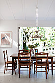 Wooden furniture in white dining room with open terrace windows leading onto balcony