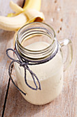 A banana milkshake in a screw-top jar with syrup and vanilla ice cream